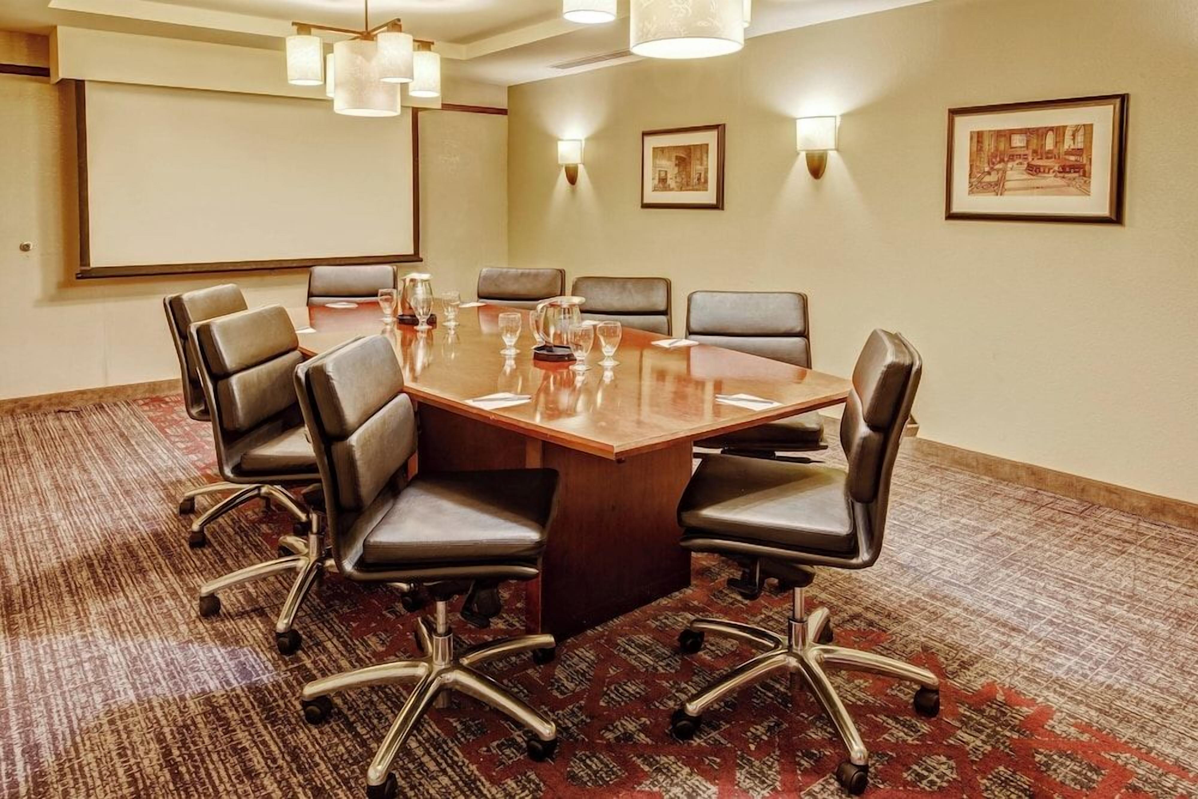 Een vergaderzaal met een grote tafel, stoelen en een projectiescherm.