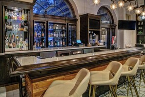 Uma área de bar com um balcão comprido, banquetas e prateleiras cheias de garrafas de bebidas.