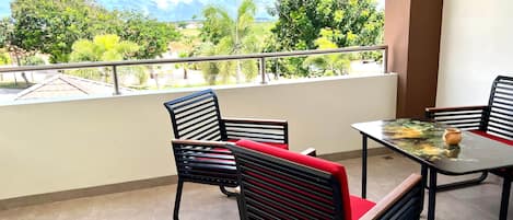 A balcony with two chairs and a table, a view of greenery and buildings, and a clear sky.