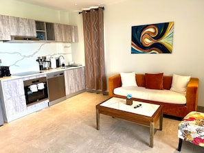 Eine moderne Küche mit Geschirrspüler, Backofen und Kaffeemaschine. Im Wohnbereich befindet sich eine Couch und ein Couchtisch.