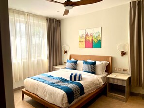A hotel room with a bed, bedside tables, a ceiling fan, a window with curtains, and a wall-mounted artwork. - C11 Xanadu Blue Bay Sleeps 2 (Sint Michiel)
