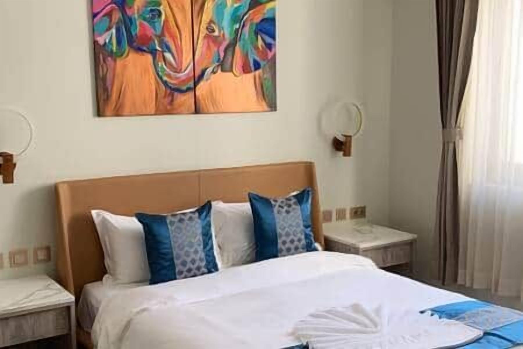 A hotel room with a bed, a nightstand, a painting on the wall, and a window with curtains.