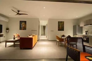 A modern living room with a sofa, a dining area with chairs, and a kitchen in the background. - C12-Xanadu Blue Bay Sleeps 4 (Sint Michiel)