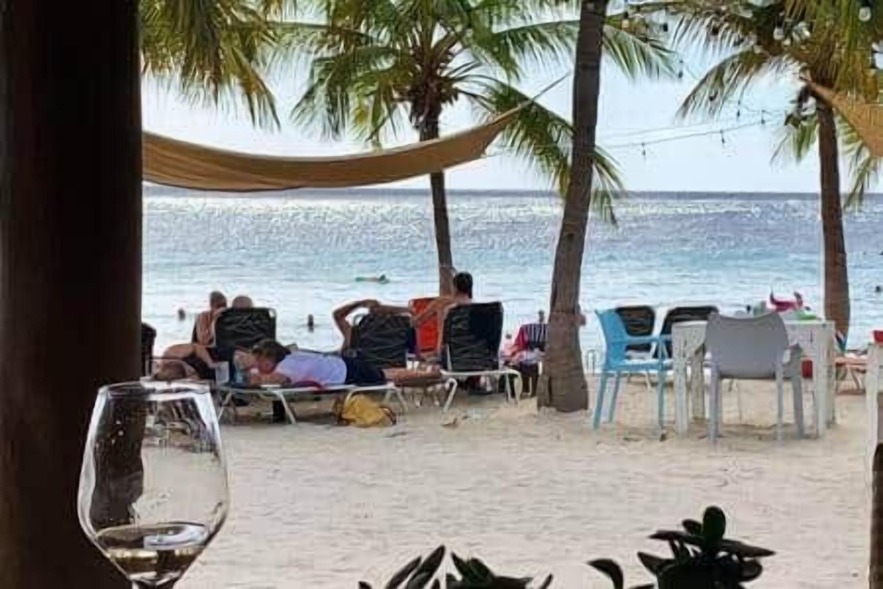 Uitzicht op het strand met een eethoek, palmbomen en strandstoelen.