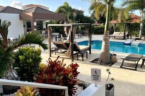 A poolside area with lounge chairs, a small palm tree, and a sign indicating a watch station. - A2-Xanadu Blue Bay Sleeps 4 (Sint Michiel)