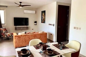 A dining area with a table set for four, a sofa, and a television in the background. - A2-Xanadu Blue Bay Sleeps 4 (Sint Michiel)