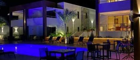 A modern building with a pool and outdoor seating area at night.