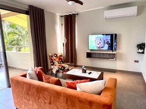 A modern living room with a sofa, a coffee table, a TV, and a balcony with curtains. - B6-Xanadu Blue Bay Sleeps 4 (Sint Michiel)