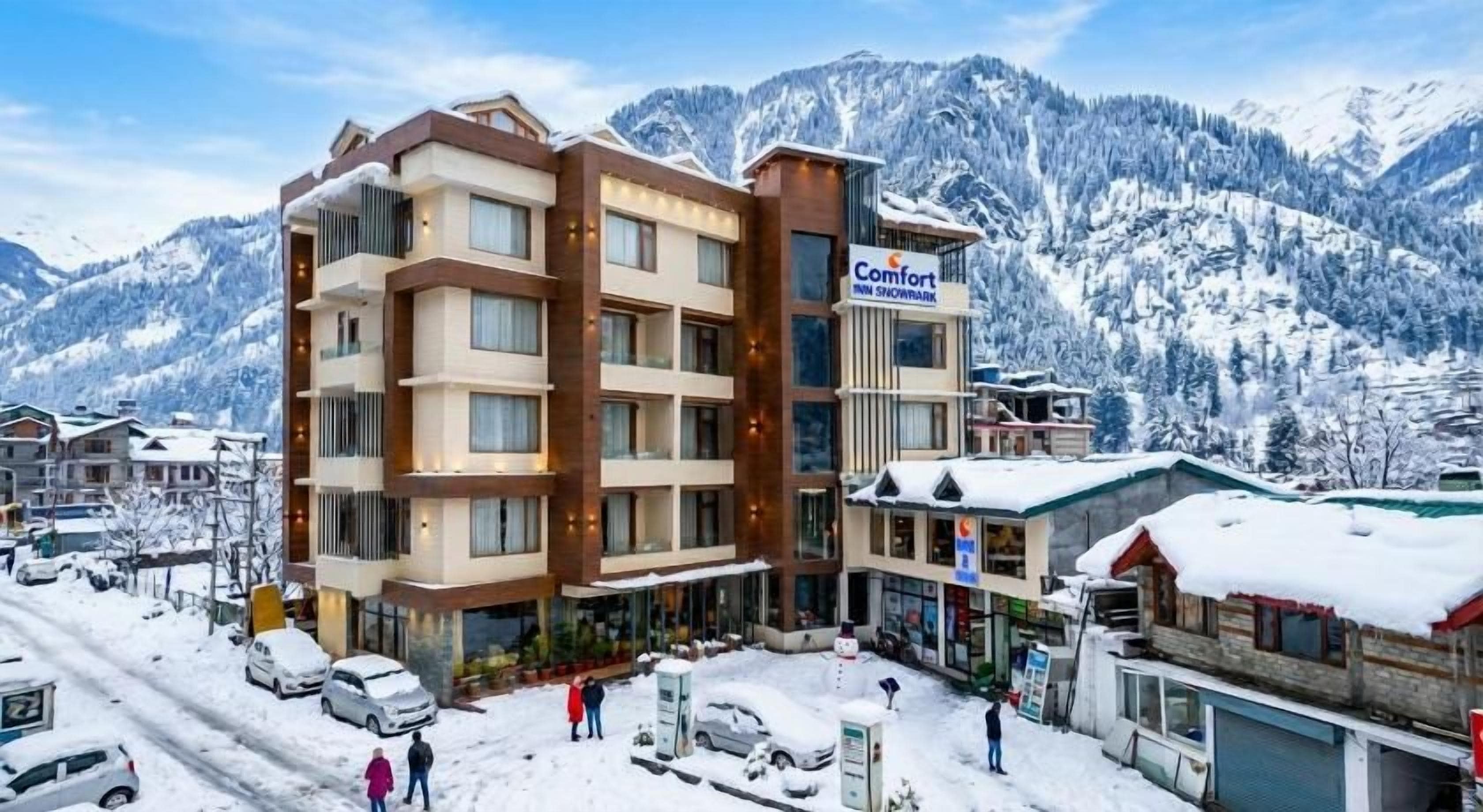 A multi-story hotel with a ski resort sign, surrounded by snow-covered mountains.