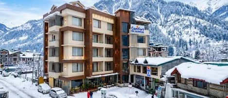 Un hotel de varios pisos con un letrero de estación de esquí, rodeado de montañas nevadas.