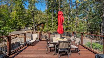 A wooden deck with a table and chairs, surrounded by a metal fence, overlooking a forested area.