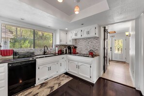 A modern kitchen with white cabinetry, a black dishwasher, and a red kettle on the counter. - Spacious 3-bedroom house in tranquil Lakehead unobstructed lake views (Lakehead)