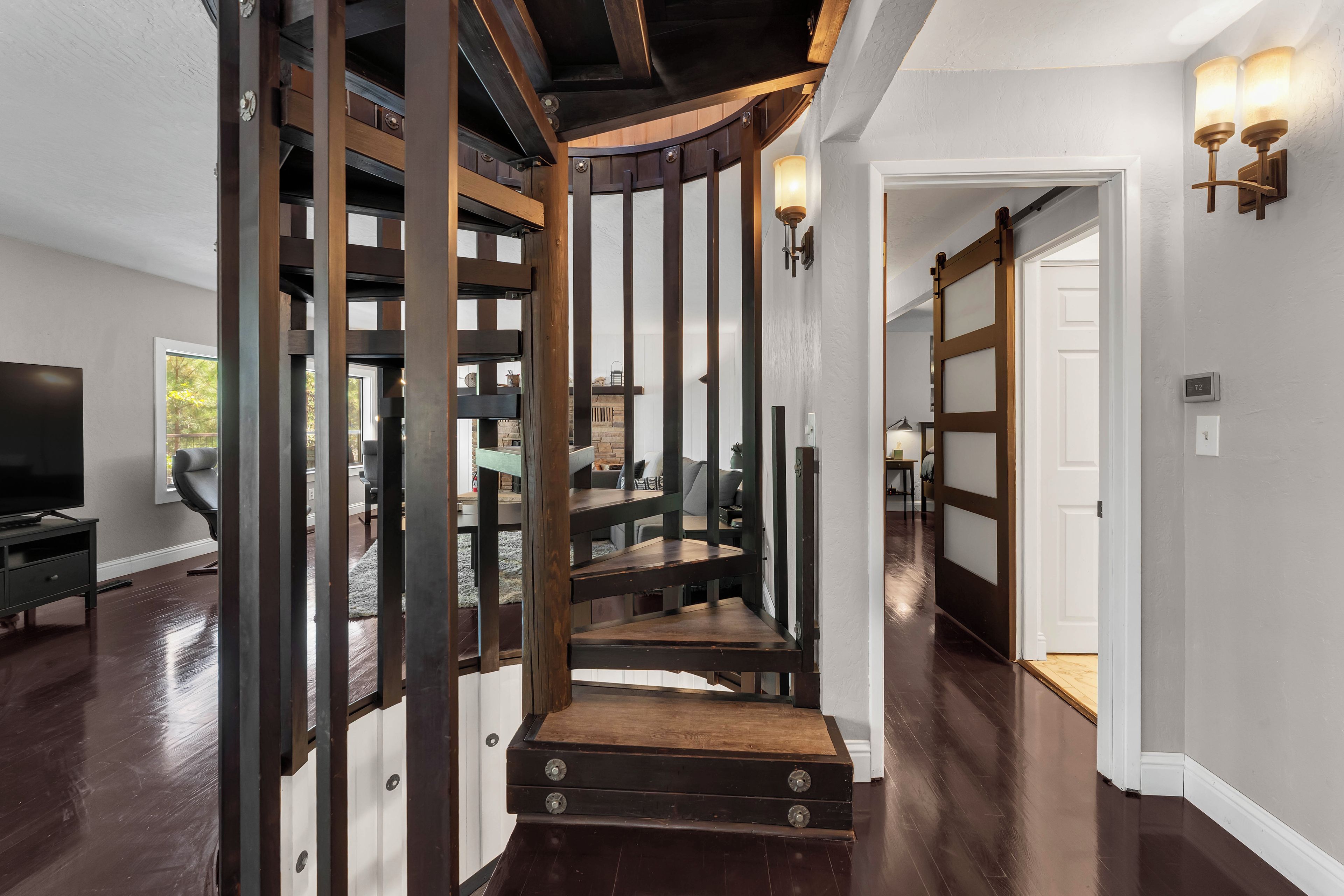 A staircase with wooden railings and a dark floor, leading to a room with a television and a window.
