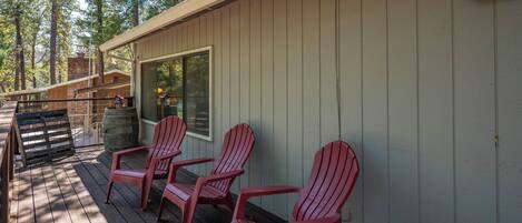 A wooden deck with red Adirondack chairs, a barrel, and a window overlooking a forested area.