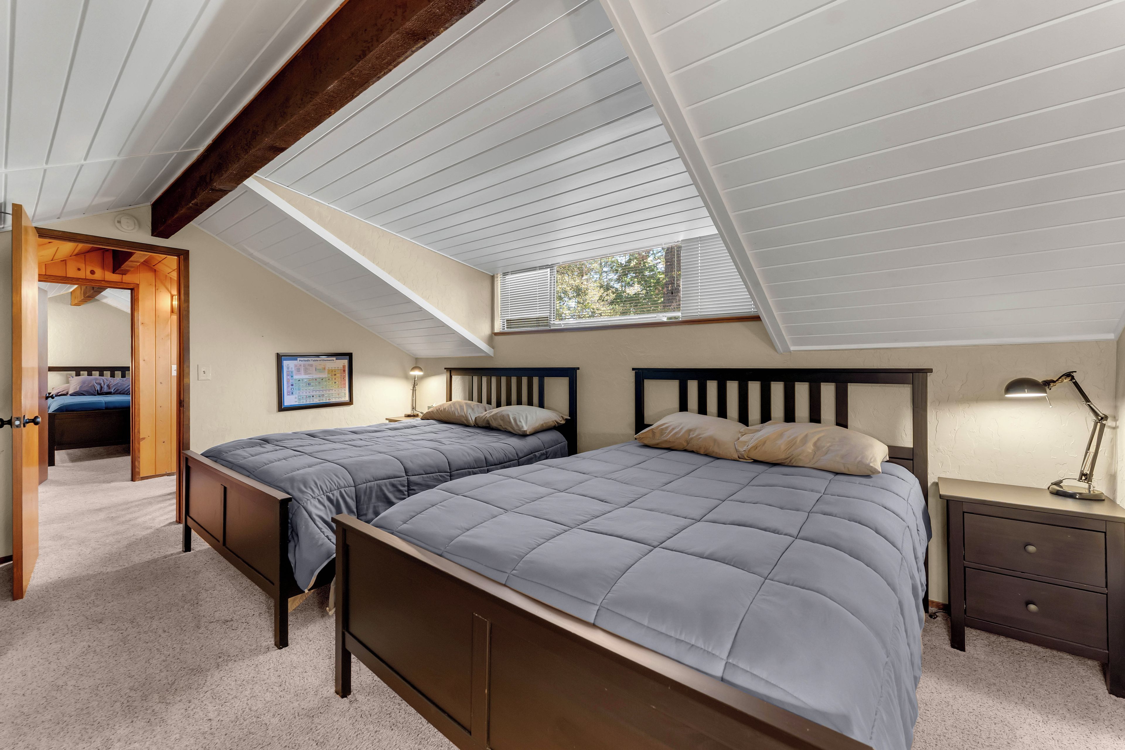 A bedroom with two beds, a skylight, a nightstand, and a framed periodic table on the wall.