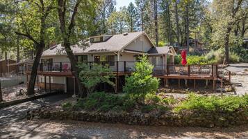 A two-story house with a deck, surrounded by trees and a stone wall.