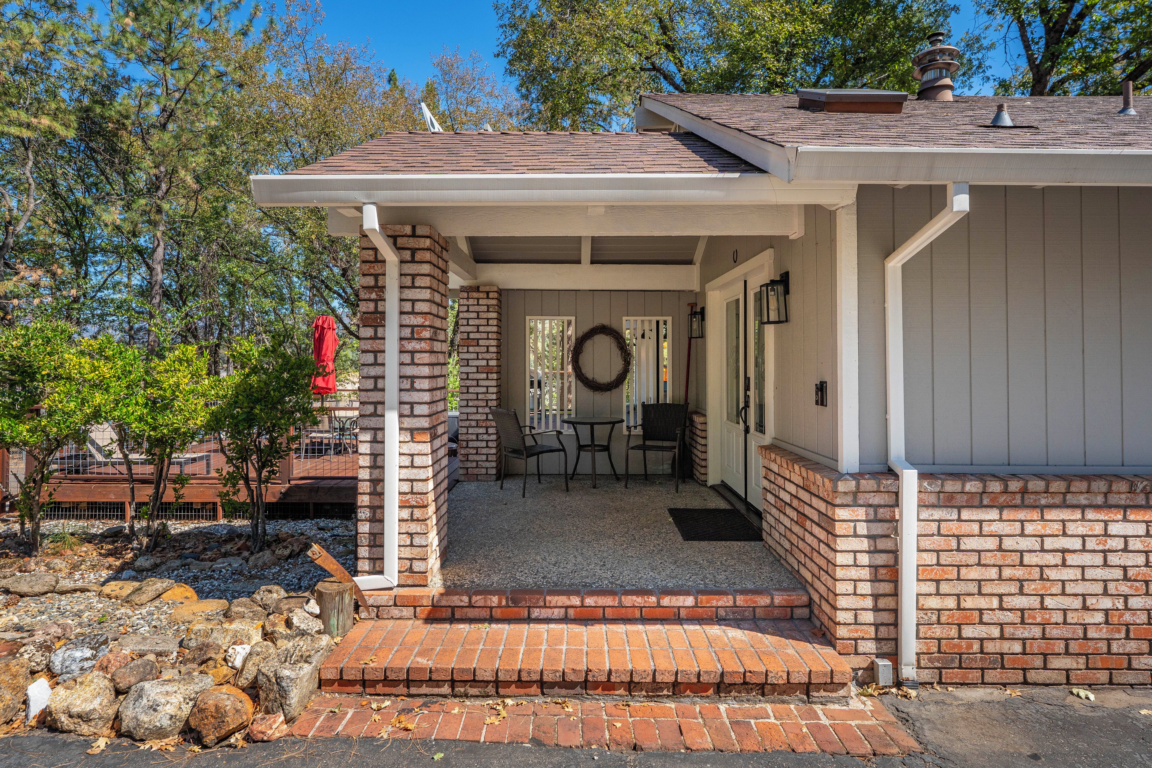 A covered porch with a brick exterior, a small table and chairs, and a wreath on the wall.