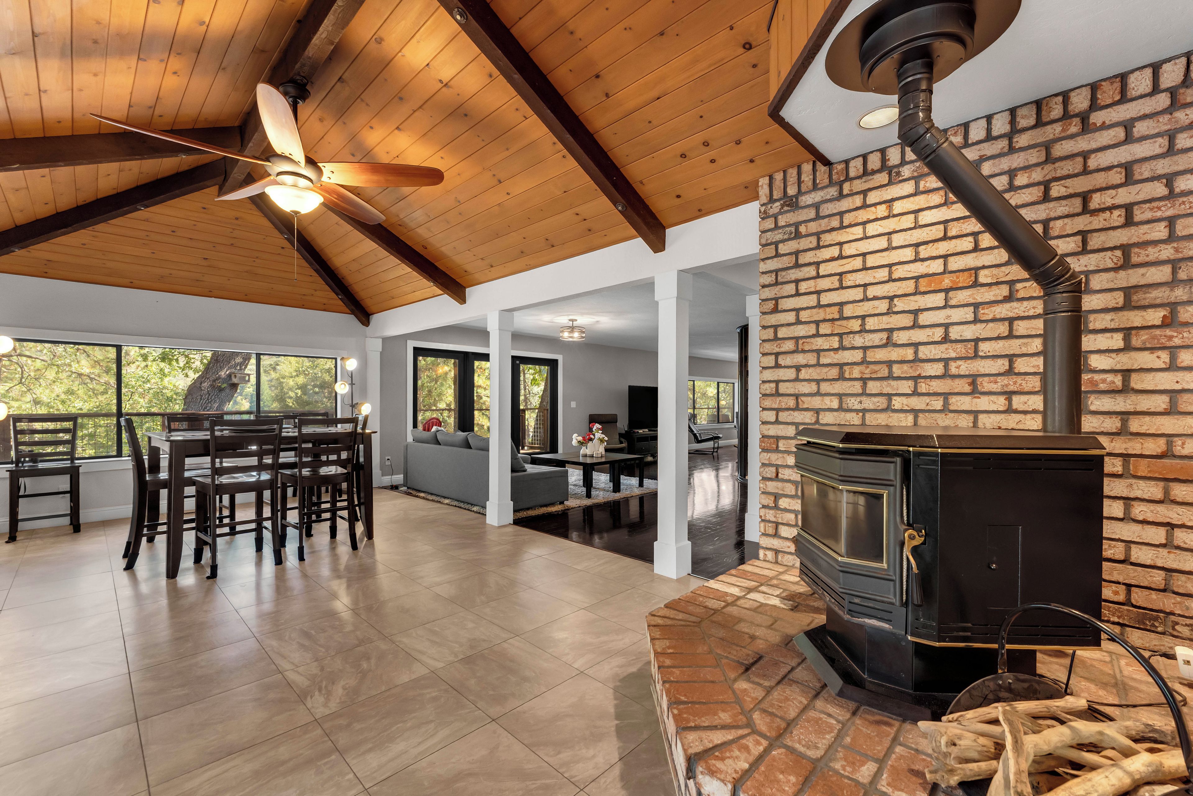 A spacious living area with a fireplace, wooden ceiling, and large windows.