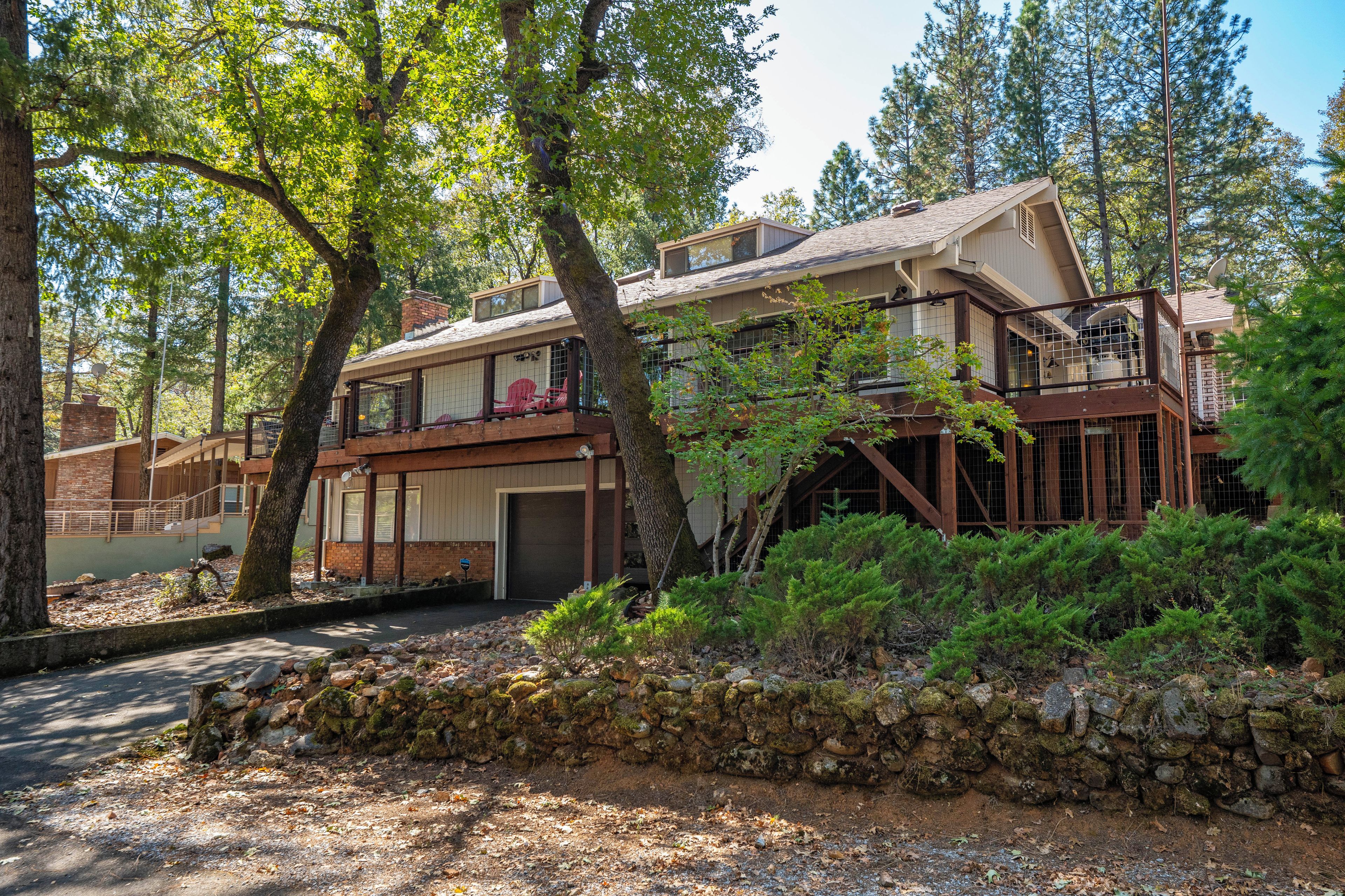 A two-story house with a garage, surrounded by trees and a stone wall.
