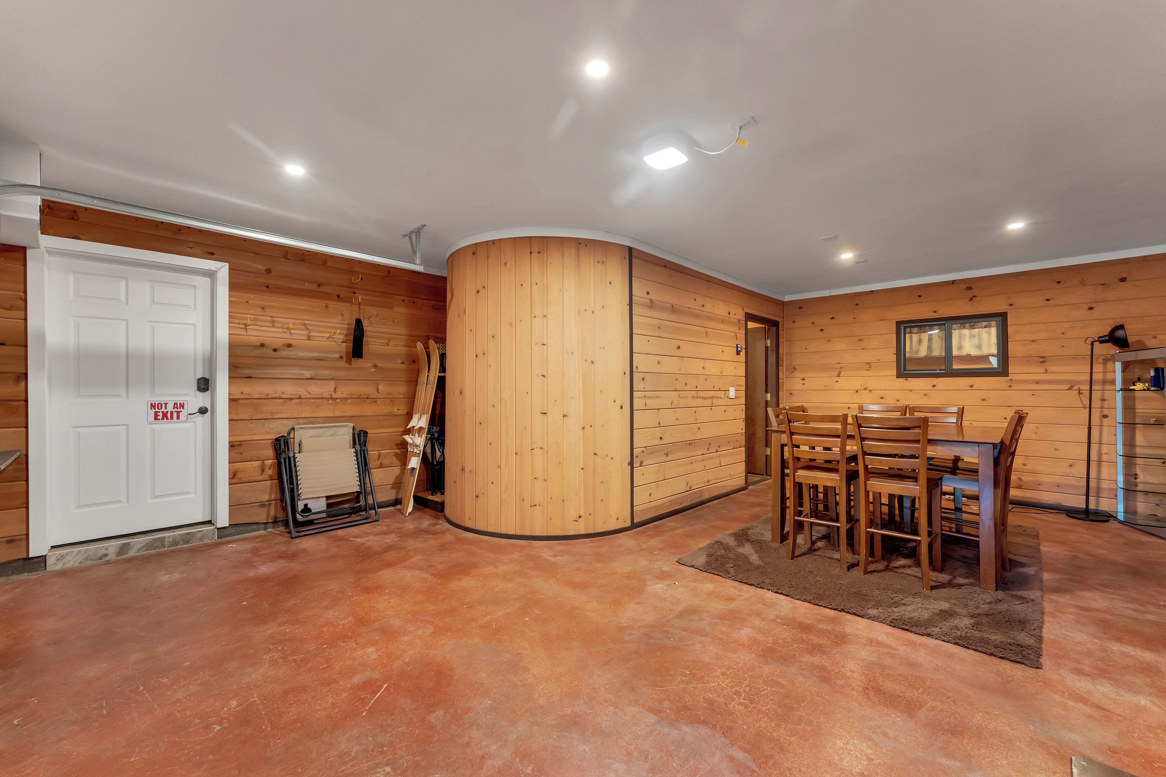 Una habitación con paredes de madera, una puerta blanca, una mesa de comedor con sillas y una lámpara en el techo.