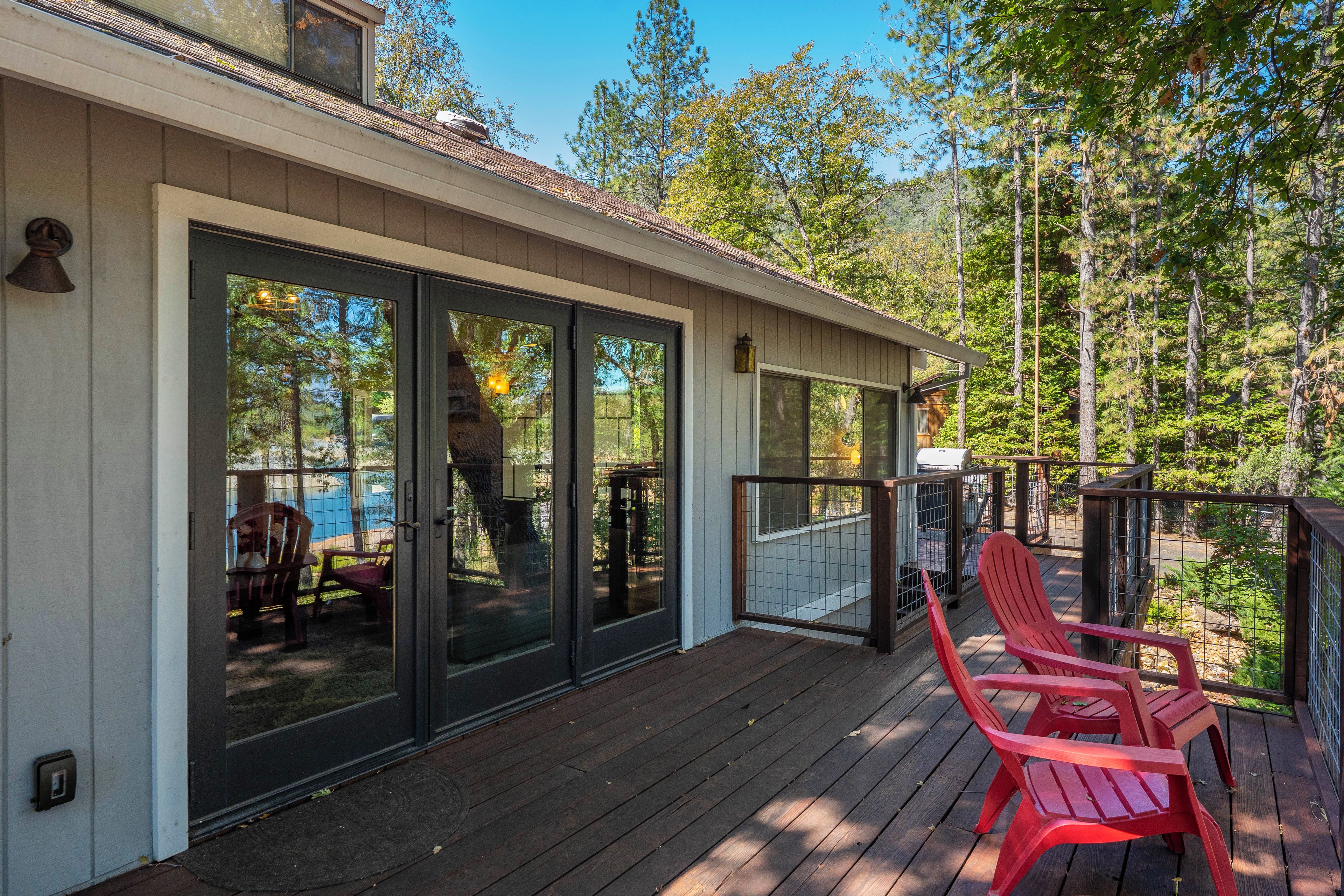 A covered deck with sliding glass doors, red Adirondack chairs, and a view of a forested area.