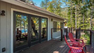 A covered deck with sliding glass doors, red Adirondack chairs, and a view of a forested area.