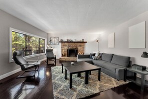 Una sala de estar moderna con chimenea, un sofá, una mesa de centro y un ventanal con vistas a árboles.