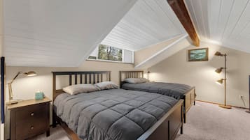 Una camera da letto con soffitto spiovente, un letto con copriletto grigio, lampade da comodino, un comodino e un quadro incorniciato appeso al muro.