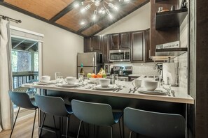 A modern kitchen with dark wooden cabinets, stainless steel appliances, and a central island with bar seating. - Steps to Shuttle | Communal Amenities (Mammoth Lakes)
