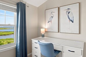 Ein Zimmer mit Schreibtisch, Stuhl, Lampe und zwei gerahmten Vogelbildern an der Wand.