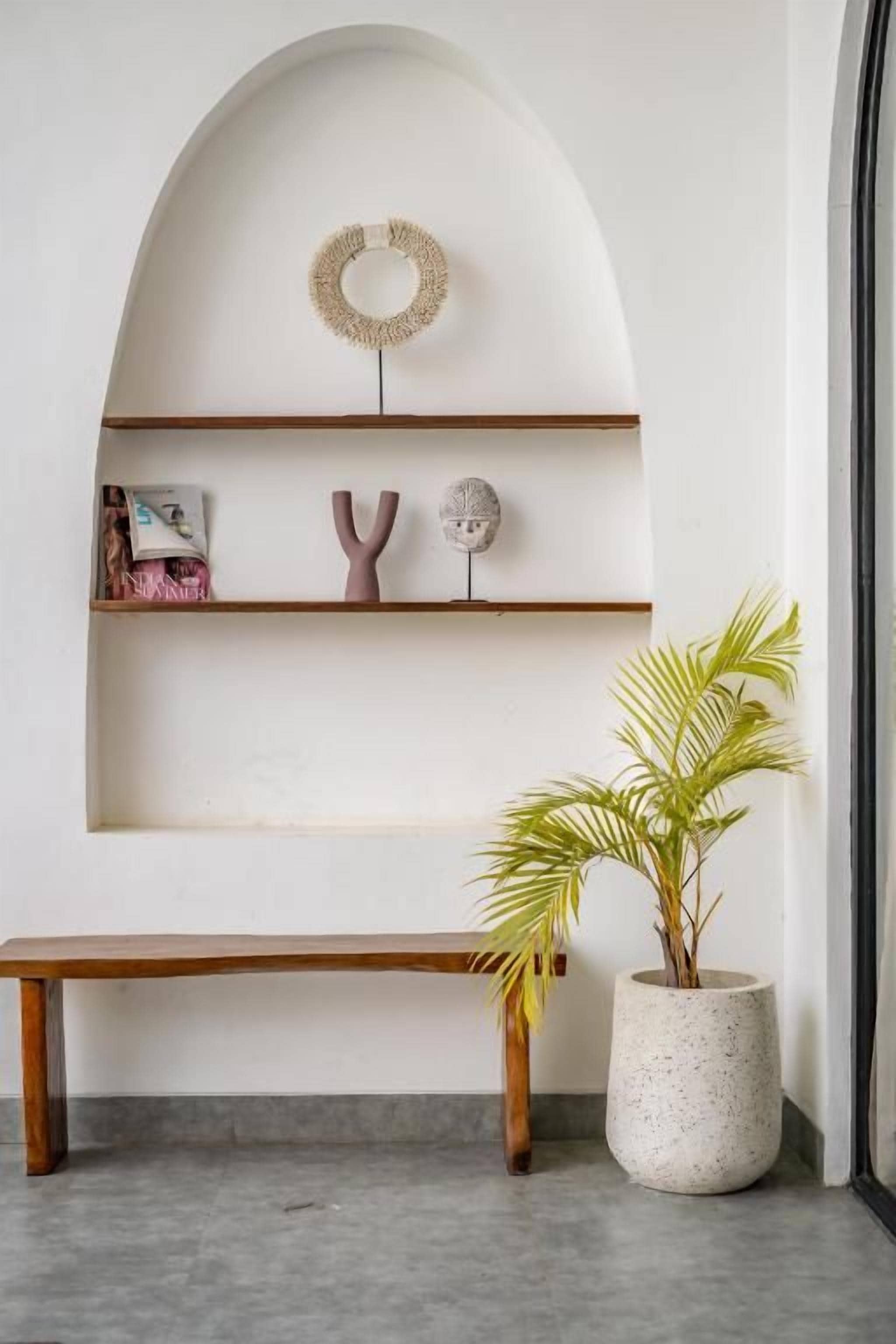 A minimalist interior with a wooden bench, a potted plant, and a wall-mounted shelf with decorative items.
