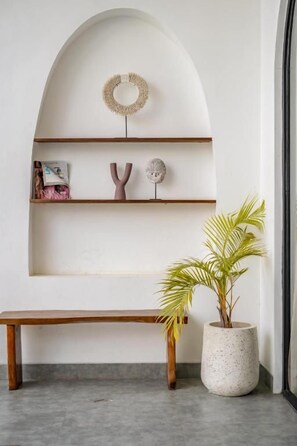 Et minimalistisk interiør med en træbænk, en potteplante og en hylde med dekorative genstande.