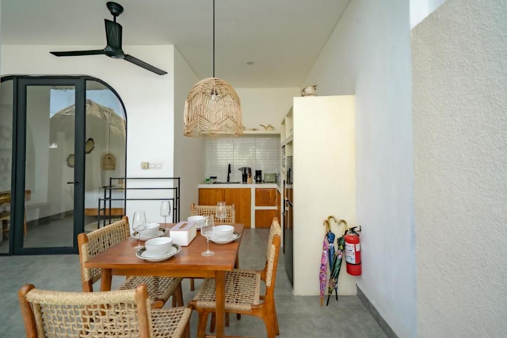 A dining area with a wooden table set for four, surrounded by wicker chairs, a ceiling fan, and a woven pendant light.