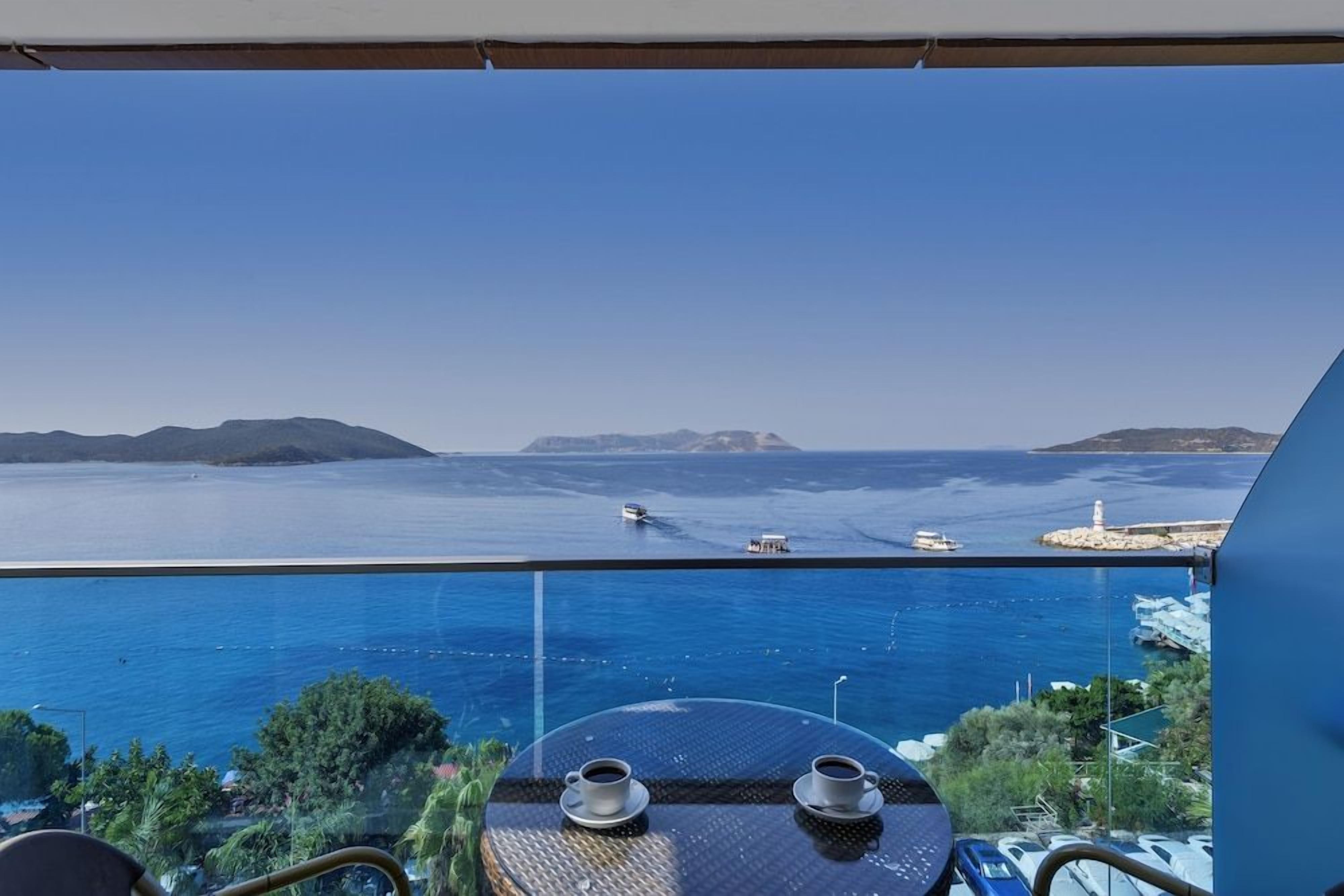 Un balcón con mesa y sillas con vistas a una masa de agua donde se ven barcos y un faro.