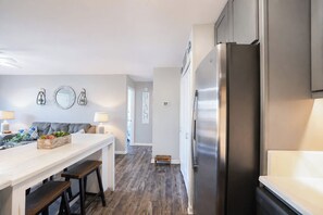 Eine moderne Küche mit einem Edelstahl-Kühlschrank, einer Holz-Kochinsel mit Barhocker und einem grauen Sofa im angrenzenden Wohnbereich.