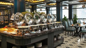 A buffet setup with multiple serving stations, a dining area with chairs and tables, and a view of the outdoors through large windows. - Holiday Sapa (Sa Pa)
