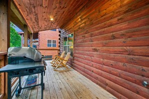 A wooden deck with a grill, chairs, and a table. - Luxury Lodge w/ Pool, Game Room & Mountain Views (Sevierville)