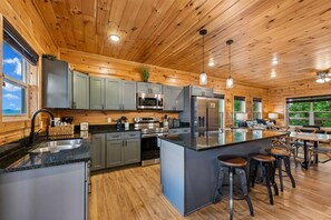 A modern kitchen with wooden walls, stainless steel appliances, and a central island with bar stools. - Luxury Lodge w/ Pool, Game Room & Mountain Views (Sevierville)
