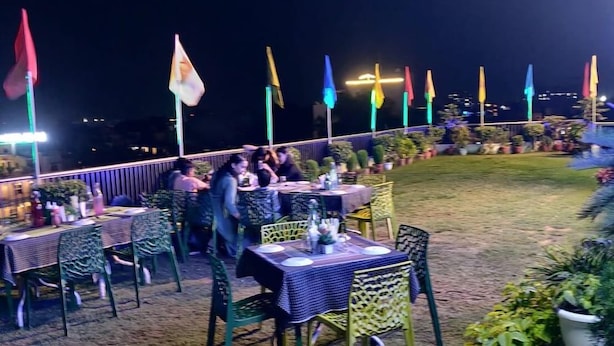 Un área de comedor al aire libre con mesas y sillas, rodeada de macetas con plantas y banderas.