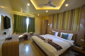A hotel room with a large bed, a bedside table, a desk, a television, and a ceiling fan. - OYO Premium Assi Ghat (Varanasi)