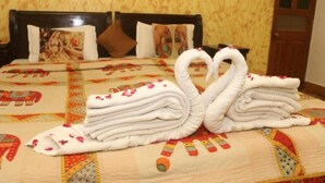 Una cama con un cabecero decorativo, un colcha con estampado floral y una presentación de toallas con forma de cisnes.