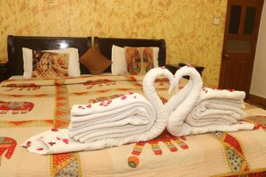 Una cama con un cabecero decorativo, un colcha con estampado floral y una presentación de toallas con forma de cisnes.
