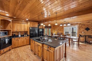 Het interieur van een blokhut met een keuken, voorzien van houten kastjes, een centraal eiland en hanglampen.