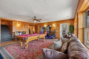 Een gezellige kamer met een pooltafel, een plafondventilator en een bank.