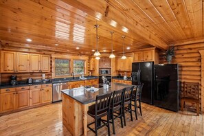 Cocina de cabaña de madera con armarios de madera, una isla central con sillas y un refrigerador negro.