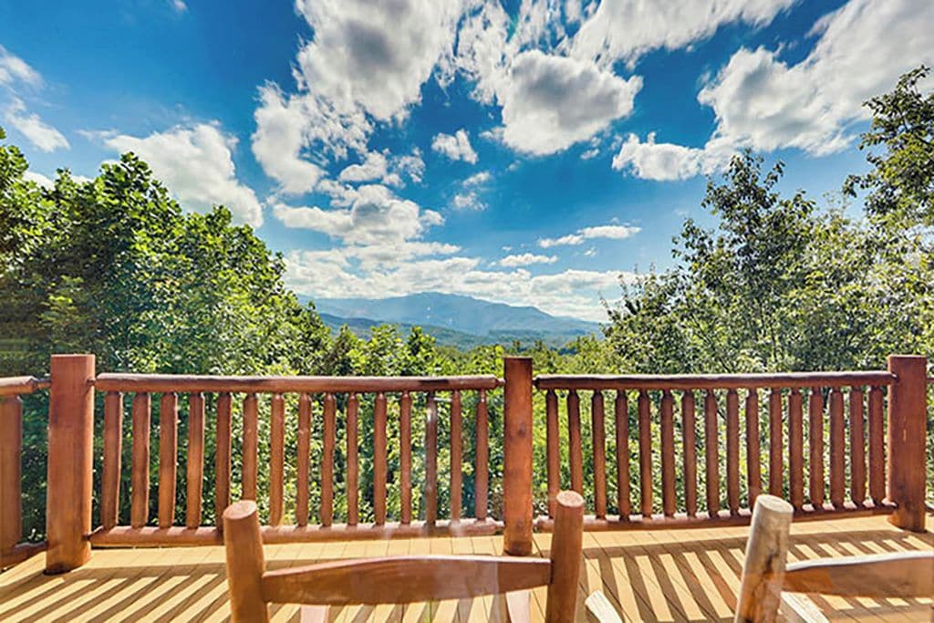 Eine Holzdar Terrasse mit Geländer mit Blick auf eine gebirgige Landschaft.