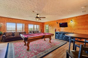 Ein Zimmer mit Poolbillard, einer Sitzecke, einem Fernseher und einem Deckenventilator.