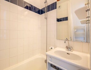 Ein Badezimmer mit weißen Fliesen, einer Badewanne, einem Waschbecken und einem Spiegel.