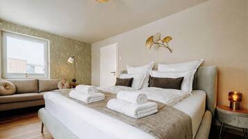 Une chambre d’hôtel comprenant un lit, un canapé, une table de chevet, une lampe et un élément décoratif mural.