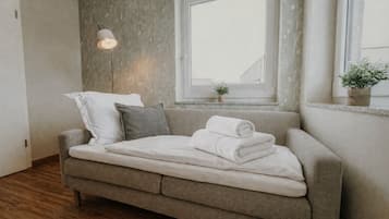 Ein sofasofa in neutralen Farbtönen mit einer weißen Decke und aufgerollten Handtüchern, einer Stehlampe und einem Fenster mit Blick auf Gebäude.